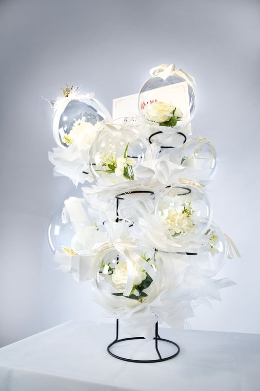 ホワイト系のバルーンフラワータワー。清楚な白い花が透明なバルーンに包まれ、華やかにディスプレイされています